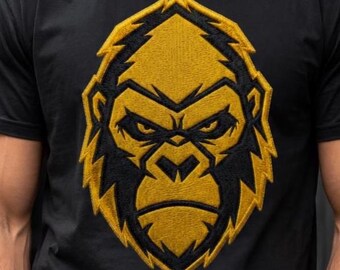 May include: A black t-shirt featuring a large, centered embroidered graphic of a gorilla head. The design uses bold yellow and black thread to create a stylized, geometric portrait of the primate with a focused, intense facial expression.