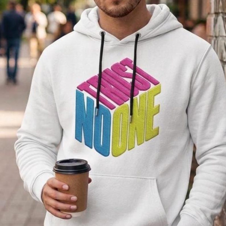 May include: A white hooded sweatshirt featuring a graphic design of a three-dimensional cube with the text "TRUST NO ONE" printed in pink, blue, and yellow. The hoodie includes a front kangaroo pocket and black drawstrings with silver metal tips.