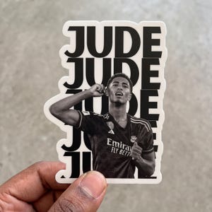 May include: A die-cut sticker featuring a black and white photograph of a soccer player in a jersey with the text Emirates Fly Better. The name JUDE is repeated in large black capital letters in the background behind the player's figure.