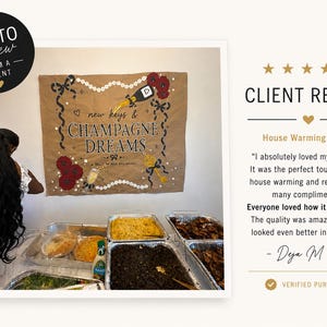 May include: A tan fabric banner featuring the text "new keys & CHAMPAGNE DREAMS" and "A TOAST TO NEW BEGINNINGS". The design includes illustrations of a champagne bottle, red flowers, a gold key, and black ribbons, displayed above a table of food.