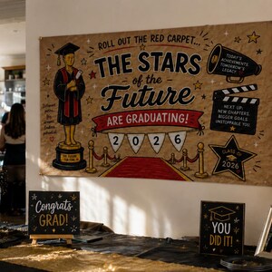 May include: A large rectangular graduation banner with a tan background featuring the text "ROLL OUT THE RED CARPET... THE STARS OF THE FUTURE ARE GRADUATING!" and "2026" on white pennants. It includes illustrations of a trophy, megaphone, and film clapper.
