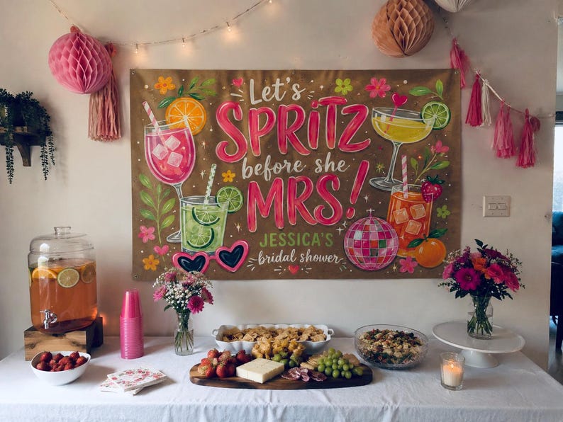May include: A rectangular banner featuring the text Let's SPRITZ before she MRS! JESSICA'S bridal shower. The design includes illustrations of colorful cocktails, a disco ball, heart-shaped sunglasses, citrus slices, and flowers on a tan background.