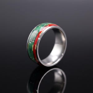 Könnte beinhalten: Ein metallischer Ring mit einer Einlage, die wie eine grüne und rote Leiterplatte aussieht. Die Außenkanten des Rings bestehen aus poliertem, silberfarbenem Metall und bilden eine glatte, reflektierende Oberfläche, die mit der Einlage kontrastiert.