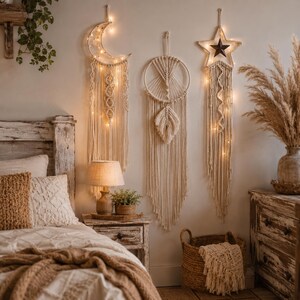May include: Three off-white macrame wall hangings featuring a crescent moon, a circular dreamcatcher, and a star shape. Each piece is crafted from cotton cord with intricate knotting and integrated warm fairy lights, suspended vertically on a wall.