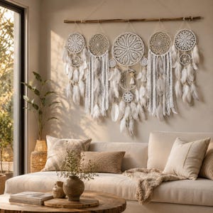 May include: A large wall hanging featuring five white crocheted dreamcatchers suspended from a horizontal wooden branch. The design includes intricate lace patterns, hanging white feathers, and long white fringe, creating a layered display.