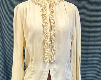 May include: A white blouse with a lace ruffle collar and long sleeves. The blouse is buttoned up the front and has a brown skirt underneath.