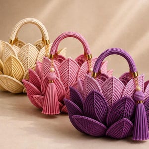 Può includere: Tre borse a mano a forma di fiori di loto, disposte in fila. Le borse sono di colore crema, rosa e viola. Ogni borsa presenta un manico arrotondato, una nappa abbinata fissata a un anello dorato e pannelli esterni a forma di petali sovrapposti.