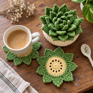 Puede incluir: Una taza de cerámica blanca llena de café sobre un posavasos de ganchillo verde y amarillo. Al lado hay una suculenta de ganchillo verde en una maceta color crema y otro posavasos de ganchillo verde y amarillo con forma de flor.