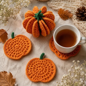 Può includere: Un set di sottobicchieri all'uncinetto a forma di zucca arancione e una zucca imbottita all'uncinetto tridimensionale. I sottobicchieri sono piatti e circolari con un gambo verde, mentre la zucca imbottita è rotonda con sezioni a coste e un gambo.