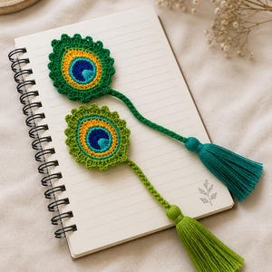 May include: Two handmade crochet bookmarks shaped like peacock feathers. Each features a central blue eye, surrounded by yellow and green concentric circles with a scalloped edge. A long braided stem extends from each, ending in a yarn tassel.