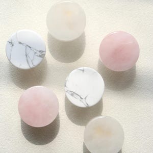May include: A collection of six circular knobs arranged in a cluster. The set includes two white knobs with grey veining, two solid pale pink knobs, and two translucent off-white knobs, all featuring a smooth, polished, rounded surface.