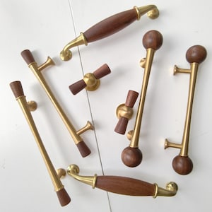 May include: A collection of cabinet hardware featuring a mix of brass and dark wood components. The set includes several long handles with wooden ends or centres, and two small T-shaped knobs, all showcasing a combination of metallic gold and brown wood.