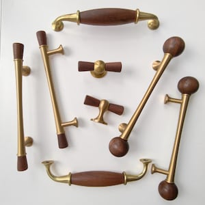 May include: A collection of cabinet hardware featuring a combination of brushed brass metal and dark brown wood. The set includes various drawer pulls and knobs with cylindrical, spherical, and elongated wooden accents and brass mounting posts.