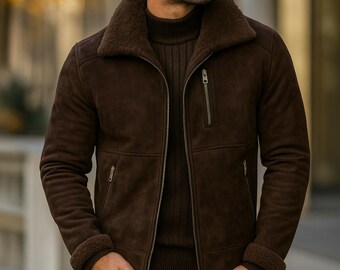 May include: A dark brown suede jacket featuring a thick, dark brown shearling collar and matching shearling cuffs. The jacket includes a full-length front zipper, a vertical zippered chest pocket, two lower zippered pockets, and a ribbed sweater underneath.