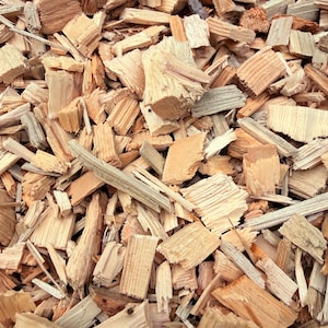 May include: A collection of light tan and beige wood chips with varying shapes and sizes. The pieces display natural wood grain textures, jagged edges, and splintered surfaces, creating a dense, layered arrangement of raw, unrefined timber fragments.