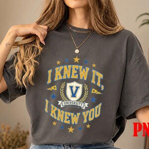May include: A charcoal grey short-sleeve t-shirt featuring a collegiate-style graphic in yellow, white, and blue. The design includes the text I KNEW IT, I KNEW YOU, a central shield with the letter V, and the word UNIVERSITY below the shield.