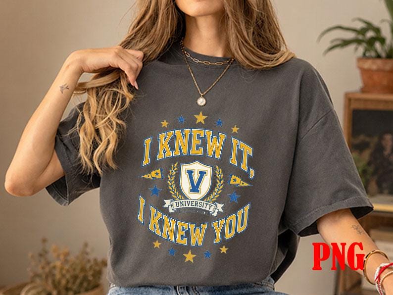 May include: A charcoal grey short-sleeve t-shirt featuring a collegiate-style graphic in yellow, white, and blue. The design includes the text I KNEW IT, I KNEW YOU, a central shield with the letter V, and the word UNIVERSITY below the shield.