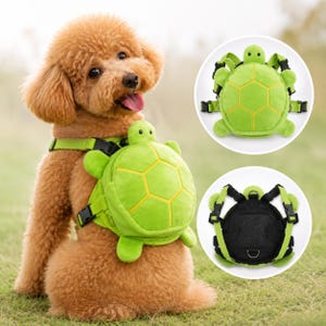 May include: A green turtle-shaped pet backpack harness featuring a plush shell design with yellow stitching, adjustable black nylon straps, plastic buckles, and a black mesh underside with a metal D-ring for leash attachment.