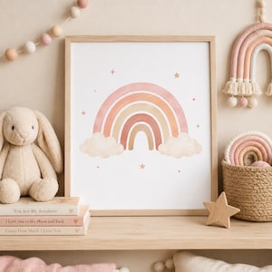 Pode incluir: Uma impressão de arte emoldurada apresentando um arco-íris em aquarela em tons de pêssego, bronzeado e creme, ladeado por duas nuvens fofas e pequenas estrelas espalhadas. A impressão é exibida em uma moldura de madeira clara.