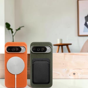 May include: Two textured leather phone cases for a smartphone with a horizontal camera bar. The left case is orange with a circular silver magnetic charger attached. The right case is olive green with a black rectangular card holder attached.