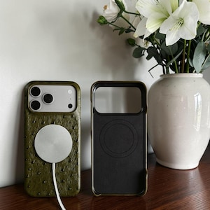 Puede incluir: Una funda de teléfono de color verde oliva con textura y patrón de puntos, que incluye un cargador magnético circular plateado en la parte posterior. Al lado hay una funda negra vacía con un diseño de anillo magnético circular en el interior.