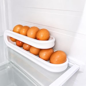 May include: A white plastic two-tiered egg storage rack holding ten brown eggs. The rack features an elongated oval shape with a curved design, allowing eggs to be organized in two rows within a refrigerator shelf space for efficient storage.