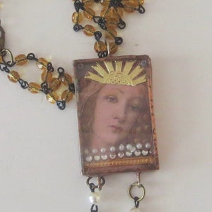 May include: A gold and brown pendant necklace with a rectangular resin cameo featuring a woman's face with a gold sunburst above her head. The cameo is surrounded by a gold trim and has a row of white pearls at the bottom. The necklace is made of brown glass beads and a black chain.