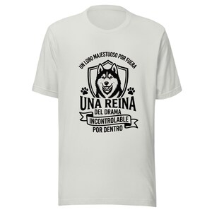 Puede incluir: Una camiseta blanca de manga corta con un gráfico negro de un lobo dentro de un escudo, flanqueado por huellas. El texto dice: UN LOBO MAJESTUOSO POR FUERA UNA REINA DEL DRAMA INCONTROLABLE POR DENTRO, en un diseño centrado y apilado.