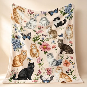 Könnte beinhalten: Eine cremefarbene Wohndecke mit einem wiederkehrenden Muster aus verschiedenen Katzen in Orange-, Grau-, Schwarz- und Weißtönen, durchsetzt mit bunten Schmetterlingen und Blumenarrangements in Rosa-, Blau- und Grüntönen auf dem gesamten Stoff.