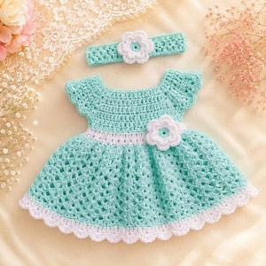 May include: A mint green and white crocheted dress featuring a short-sleeved bodice, a flared skirt with a scalloped hem, and a large white flower accent at the waist. A matching mint green crocheted headband with a white flower is included.