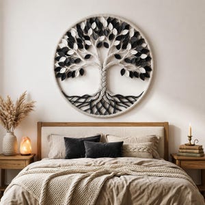 May include: A circular wall hanging featuring a braided rope tree design with black and white felt leaves. The tree trunk and branches are constructed from thick, twisted cream-colored cord, while the roots are made of black cord.