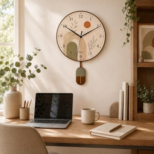 May include: A round wall clock with a cream-coloured face featuring black numerals, a dark orange sun, green arch shapes, and botanical leaf illustrations. The clock has black hour and minute hands and a rectangular pendulum with a green and wood finish.