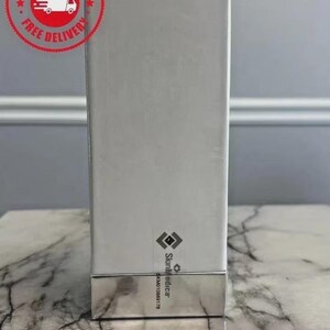 Op de afbeelding: Een rechthoekige witte productdoos met een metallic zilveren basis. De doos is voorzien van een klein zwart logo en de tekst SkinMedica verticaal gedrukt bij de onderkant, samen met de alfanumerieke code SKM010889178 onder de merknaam.