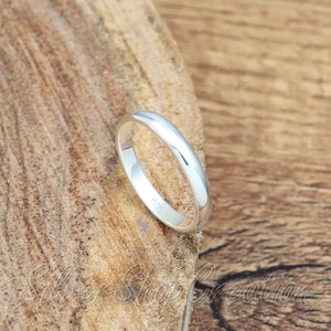 May include: A polished silver band ring with a smooth, rounded profile. The interior of the band features a clear 925 hallmark stamp, indicating sterling silver composition. The ring has a simple, solid construction with a reflective metallic finish.