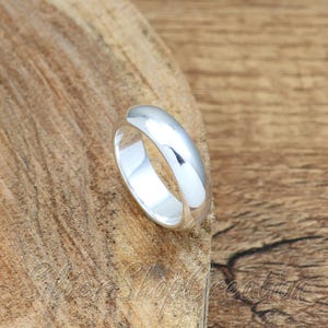 May include: A polished, smooth, solid silver band ring with a rounded profile and a high-shine reflective finish. The ring features a simple, continuous circular design with no additional embellishments, stones, or engravings on the surface.