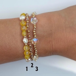 May include: Three beaded bracelets labeled 1, 2, and 3. Bracelet 1 features yellow faceted beads and white pearls. Bracelet 2 consists of small metallic gold and brown beads. Bracelet 3 includes clear star-shaped beads and metallic gold beads.