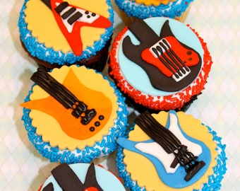 May include: Six cupcakes decorated with colorful fondant guitar designs. The cupcakes are topped with blue, red, and white sprinkles.