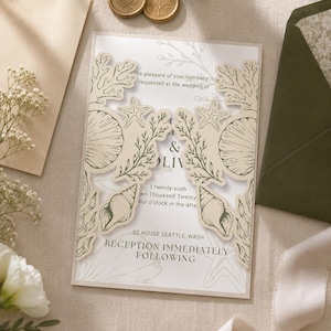 May include: A wedding invitation card featuring a laser-cut cream-colored gatefold cover with intricate illustrations of coral, seashells, and starfish. The inner white card displays black printed text detailing a wedding ceremony and reception.