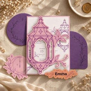 May include: A rectangular wedding invitation card featuring a die-cut pink lantern overlay with floral accents. The card includes text reading Saturday 13 August 2025, The Vine, and Emma. Accompanied by purple circular and arched cardstock inserts.