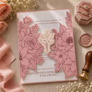 May include: A wedding invitation card featuring intricate laser-cut dusty rose floral panels that fold inward. The center displays a small floral bouquet illustration and printed text. Accompanying items include a velvet ring box and a wax seal stamp.