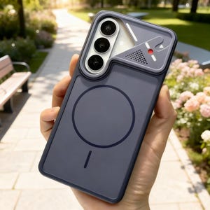 Puede incluir: Una funda de smartphone azul oscuro con un anillo de carga magnético circular en la parte posterior y una cubierta para el módulo de cámara. La sección superior incluye un diseño geométrico con un punto rojo, una rejilla y líneas blancas.