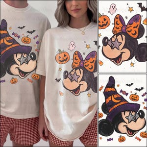 Puede incluir: Una camiseta color hueso con el gráfico de un ratón de dibujos animados que lleva un sombrero de bruja morado y naranja con una luna creciente, ojos en forma de estrella, rodeado de pequeñas calabazas, fantasmas, murciélagos y dulces.