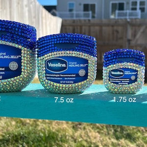May include: Four jars of Vaseline Original Healing Jelly, embellished with blue and iridescent rhinestones. The jars are labeled with their sizes: 13 oz, 7.5 oz, 1.75 oz, and .25 oz. The jars are arranged on a turquoise surface.
