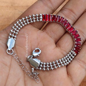 Könnte beinhalten: Ein silberfarbenes Armband mit einem Abschnitt aus drei Reihen kleiner Metallperlen und einem Abschnitt aus leuchtend roten Baguette-Steinen. Das Schmuckstück verfügt über einen Karabinerverschluss und eine Verlängerungskette mit dem Text SilverArtisan27.