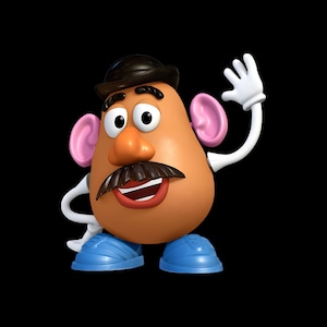 May include: A potato-shaped toy figure with a brown body, wearing a black bowler hat, a dark brown moustache, and blue shoes. The figure has pink ears, white gloves, and a smiling mouth with visible teeth, with one arm raised in a wave.