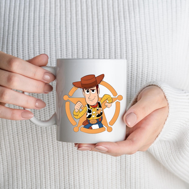 May include: A white ceramic mug featuring a colourful graphic of the character Woody from Toy Story. The character wears a brown cowboy hat, a yellow plaid shirt with a cow-print vest, and a gold sheriff badge centred on an orange star emblem.
