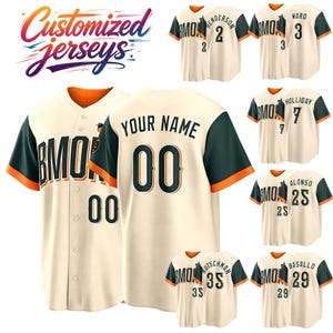 May include: A collection of cream-colored baseball jerseys featuring dark green sleeves with orange trim. The jerseys display the text BMORE, player names, and numbers in dark green with orange outlines. The text Customized jerseys is visible.