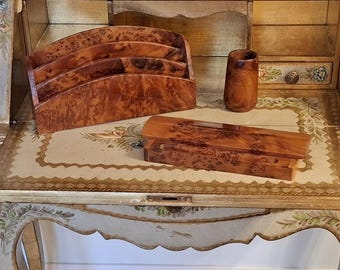 Könnte beinhalten: Ein cremefarbener Sekretär mit Klappfront, handgemalten Blumenmotiven und Goldverzierungen. Der Schreibtisch enthält einen Briefständer aus Wurzelholz, eine passende rechteckige Schatulle und einen kleinen zylindrischen Holzbecher.