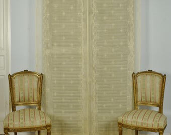 Könnte beinhalten: Zwei passende Stühle mit goldfarbenen Holzrahmen sowie gepolsterten Sitzen und Rückenlehnen mit vertikalen Streifen in Creme und gedecktem Rot. Hinter den Stühlen hängt ein langer, transparenter, cremeweißer Vorhang mit zartem Stickmuster.