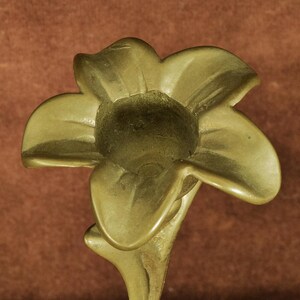 K&ouml;nnte beinhalten: Ein Kerzenhalter aus Messing in Form einer f&uuml;nfbl&auml;ttrigen Blume. Das Metall hat eine glatte, matte Oberfl&auml;che mit einem goldenen Farbton. Die Mitte der Blume weist eine kreisf&ouml;rmige &Ouml;ffnung auf, die f&uuml;r eine Stabkerze ausgelegt ist.